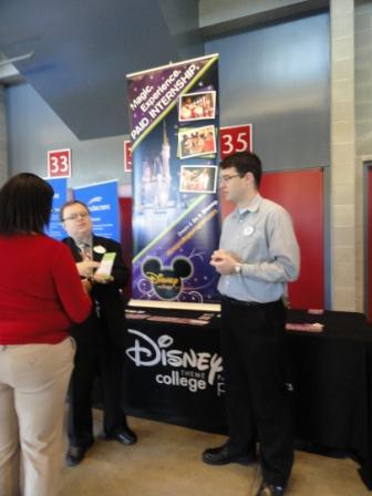 Three people talking next to a Disney College banner.
