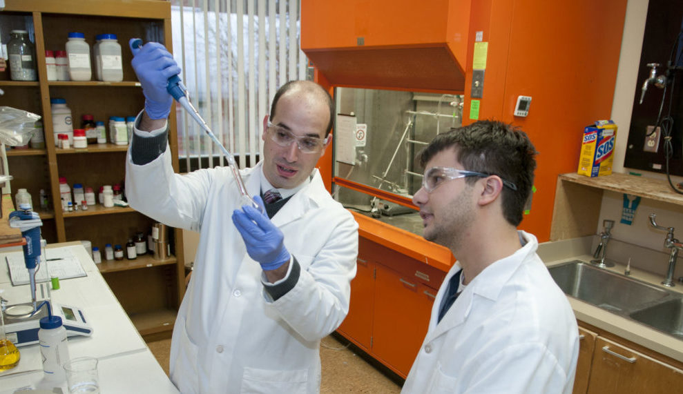 Steven Saunders adds a chemical to a beaker while a student observes.