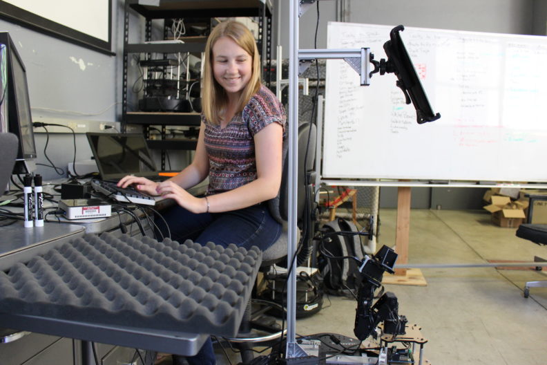Woman at a keyboard watching a robot.