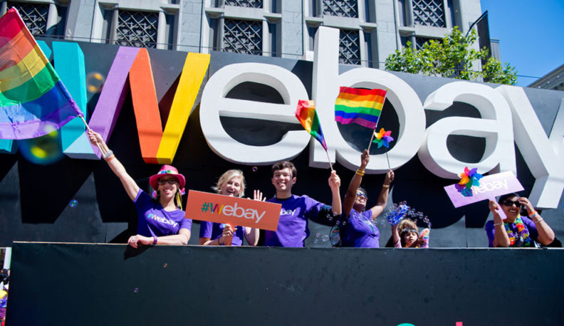 Six people in purple shirts wave pride flags in front of a #webay sign.