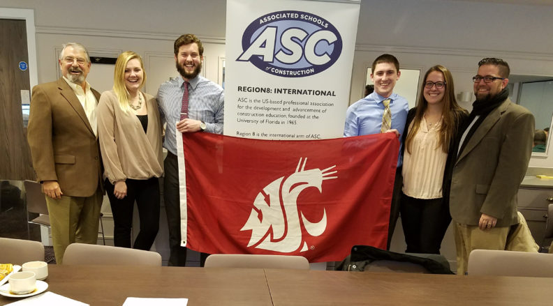 Six people pose with the WSU Cougar flag and an Associated Schools of Construction banner.