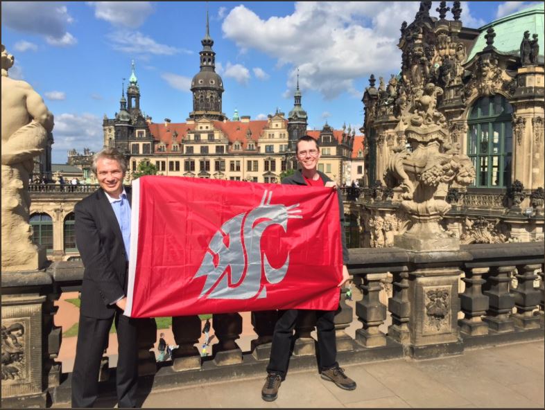 Two men holding a WSU Cougar flag up between them.