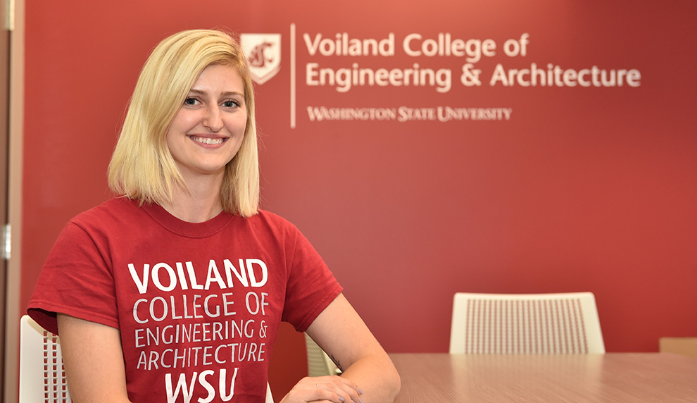 Heidi Lyons wearing a Voiland College t-shirt in front of a wall with the Voiland College logo.