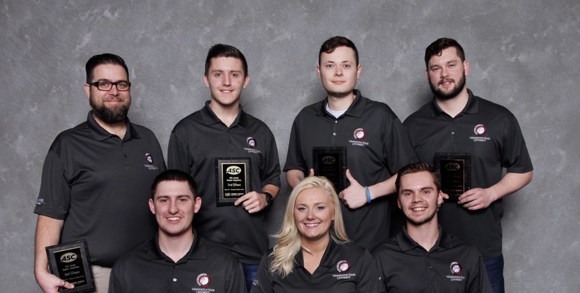 Seven people pose in two rows holding award plaques.