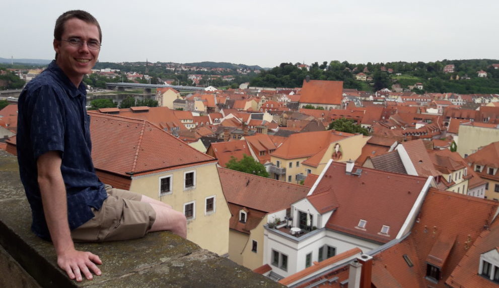 Andrew Raub sitting on an old wall overlooking rooftops.