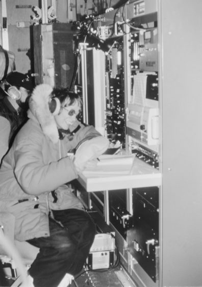 Woman wearing winter gear seated in front of research equipment.