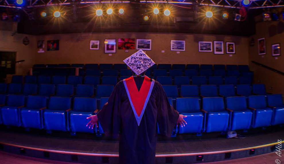 Person, back to camera, wearing a graduation cap with the text I am inimitable, I am an original.