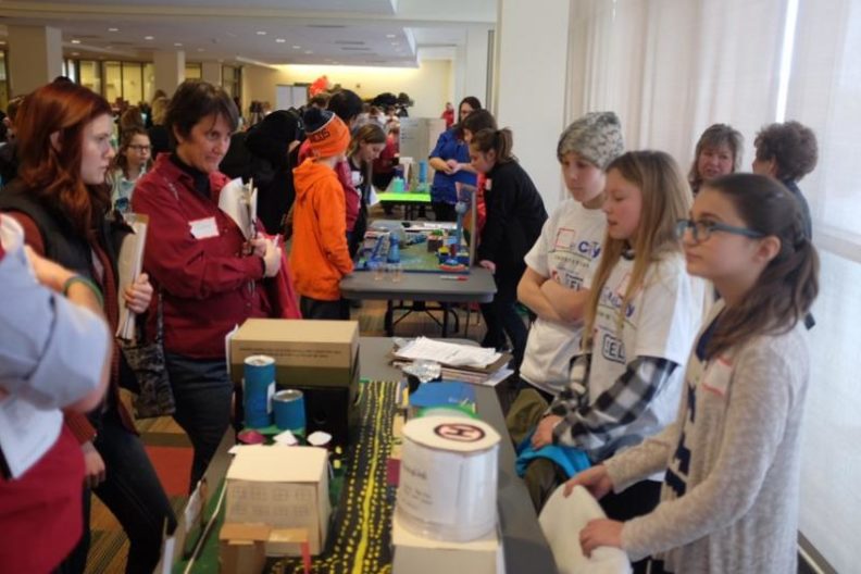 Students standing behind their models while judges evaluate them.