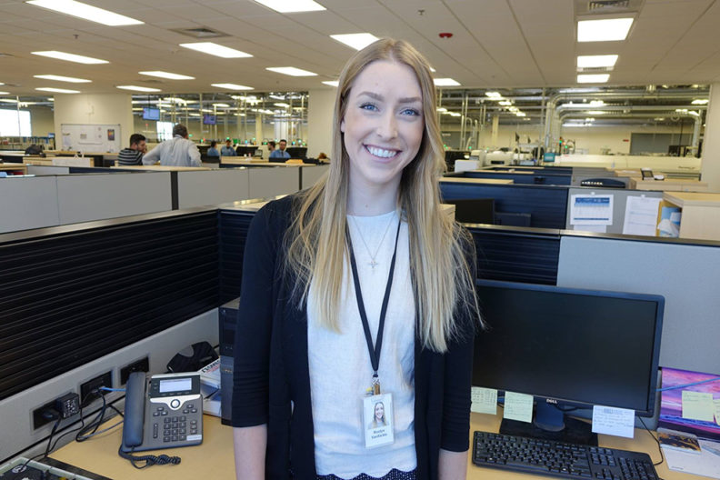 Roslyn VanSickle standing in a cubicle in a large office setting.