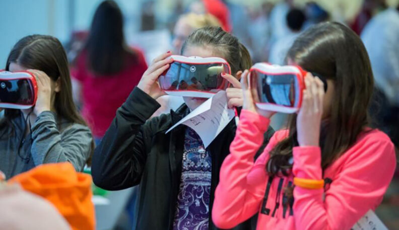 Three young girls looking through virtual reality goggles.