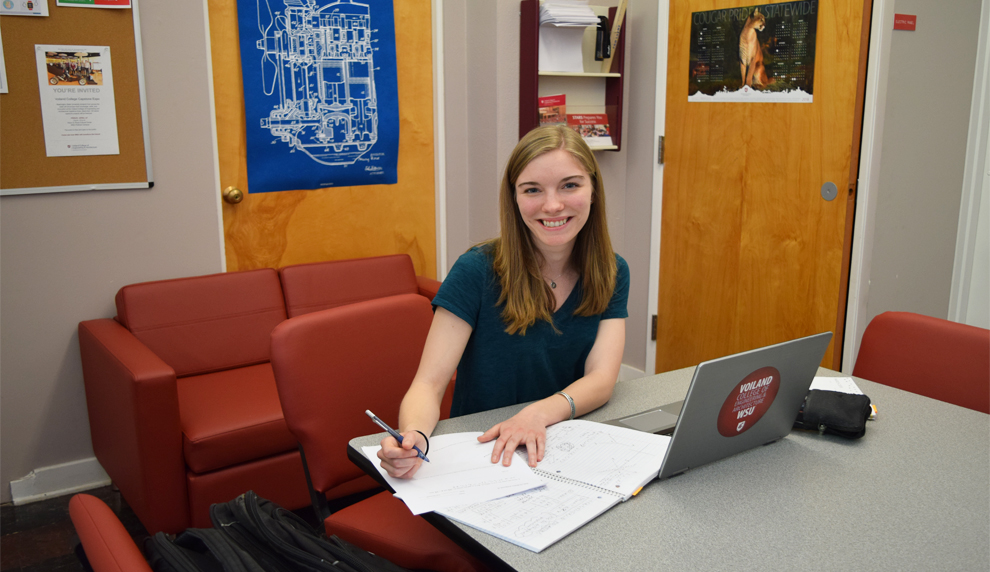 Shelby sits at desk with laptop, paper and pen.