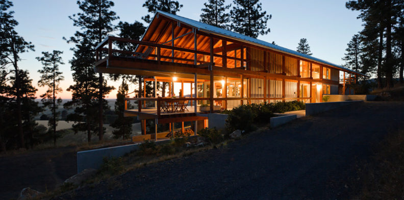 House nestled among trees at sunset with lights shining inside.