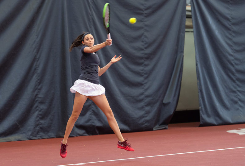 Melisa Ates jumps and swings her racket at the ball on the tennis court.