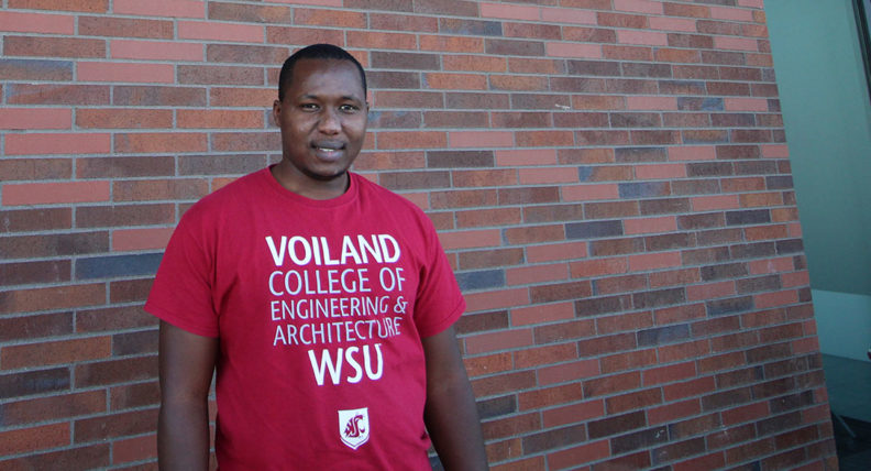 Peter Mugo stands in front of a brick wall wearing a Voiland College t-shirt.