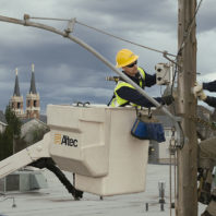 Lineman in aerial bucket assists pole-climbing lineman with installing sensors on light pole.