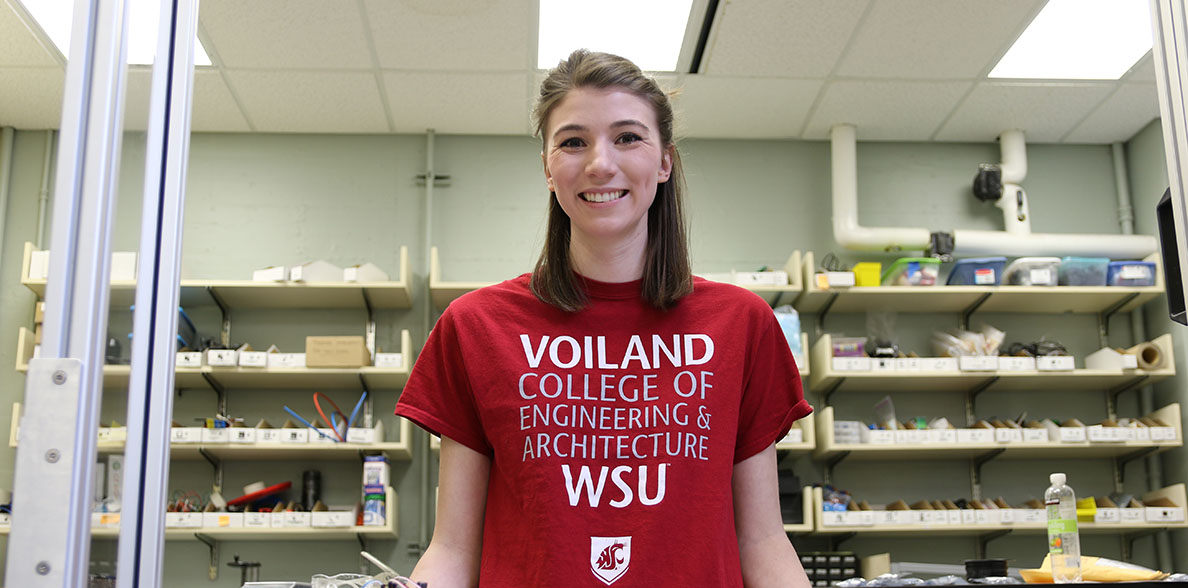 Madison Newberry wearing a Voiland College t-shirt in front of a wall of project supplies.