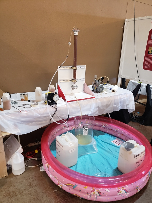 An wastewater treatment system on a table hooked to containers in a pink inflatable pool on the floor below it.