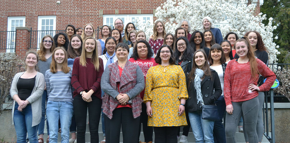 Two dozen members of the Society of Women Engineers pose for a group photo on stairs outside a building.