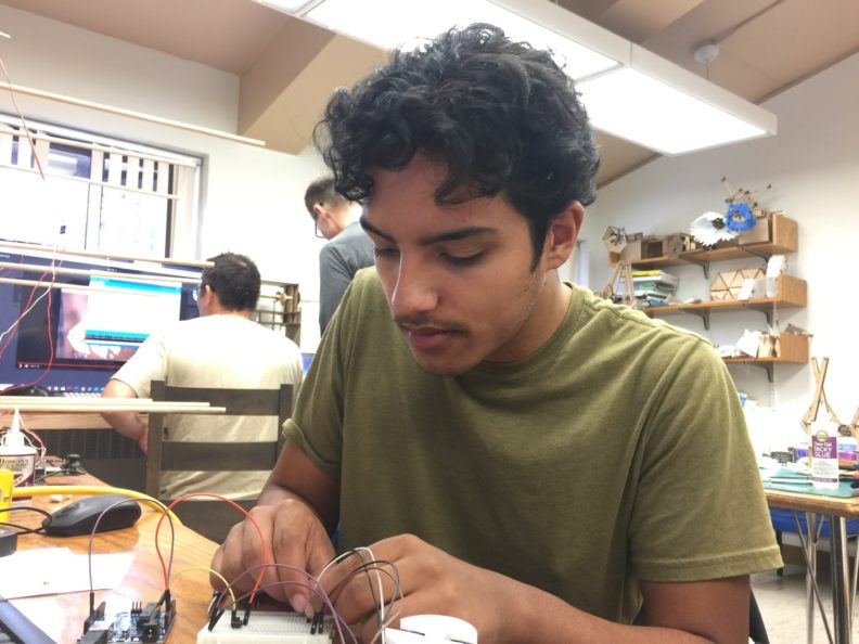 Reece Keller sitting at a table, bent over and examining a circuit board.