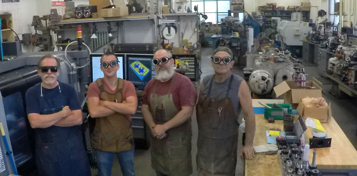 Four engineering shops workers wearing safety goggles and aprons. 