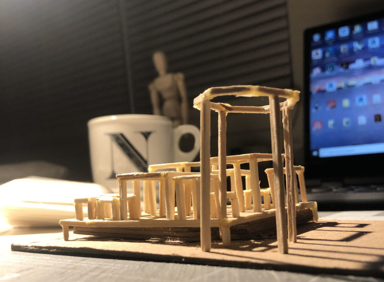 Architecture model with a coffee mug and a computer screen in the background.
