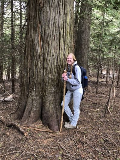 Woman in forest wearing backpack and holding walking stick.