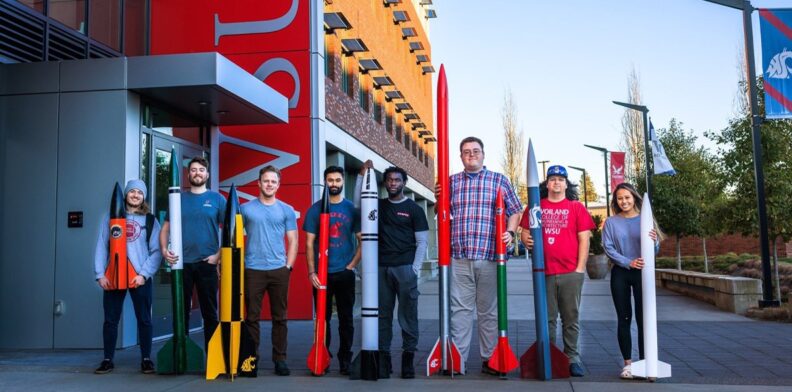 The WSU team competing in NASA's rocket launch competition posing with various rockets.