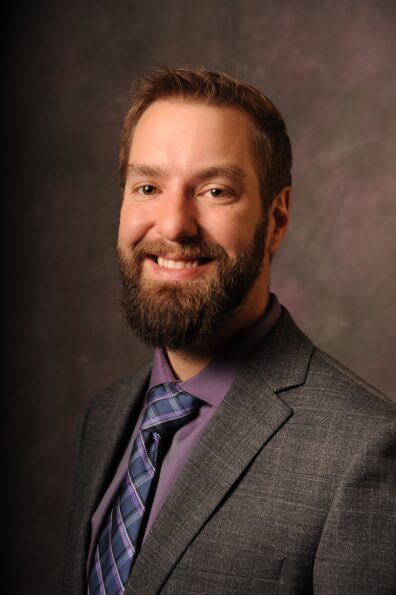 Dan Richer wearing a grey suit and purple shirt.