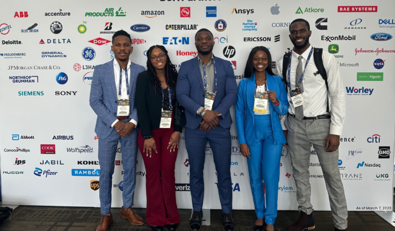 Five students pose in front of a display of convention sponsor logos.