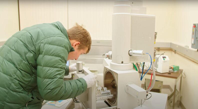 Man wearing cold-weather coat looking into lab equipment.