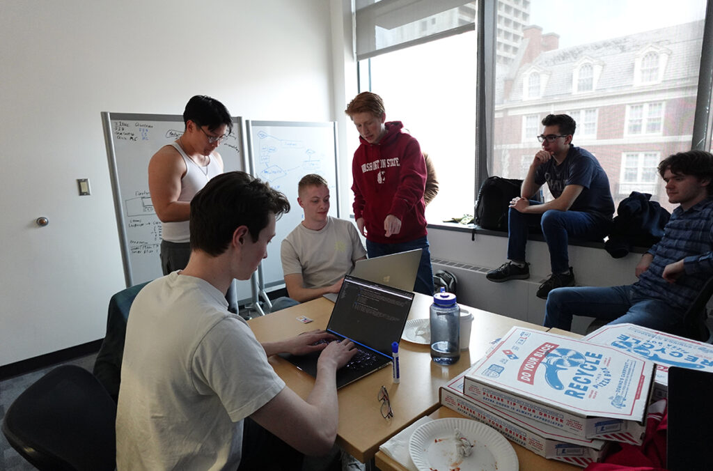 Students eat pizza while working on laptops.