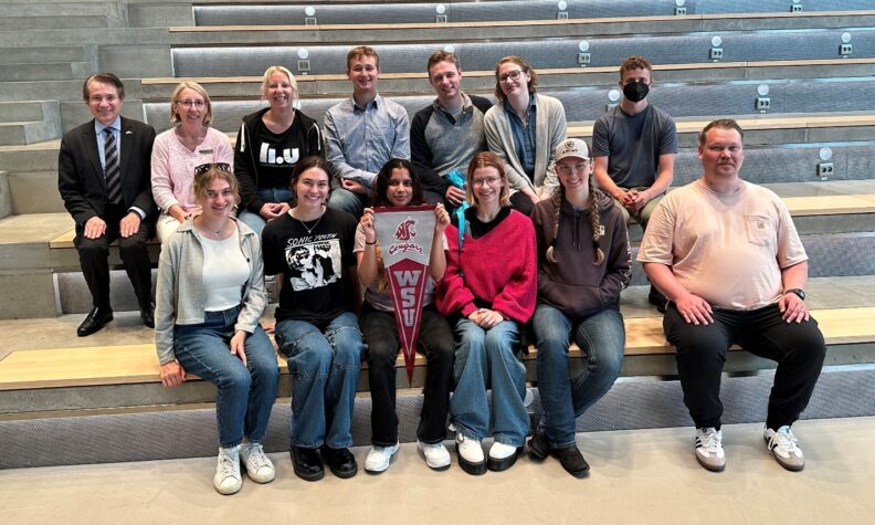 Students pose on stadium seating. One holds a WSU Cougar pennant.