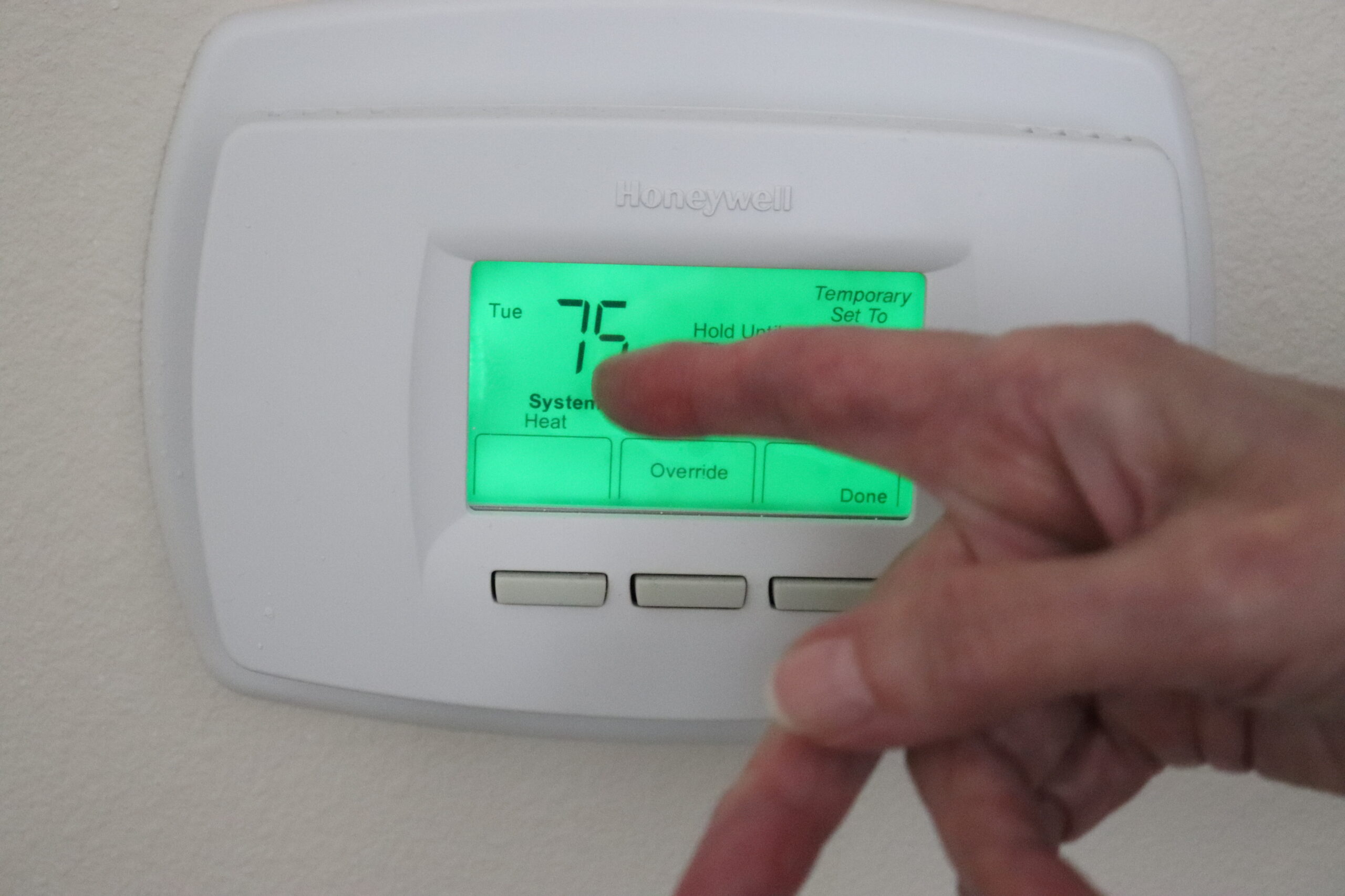 Elderly hand pointing at the screen of a digital thermostat.