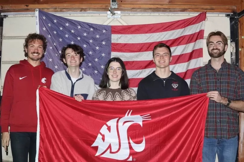 Five people holding up a WSU Cougar flag while standing in front of of a USA flag.