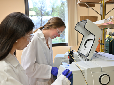 Two students wearing white lab coats in a chemical engineering lab.