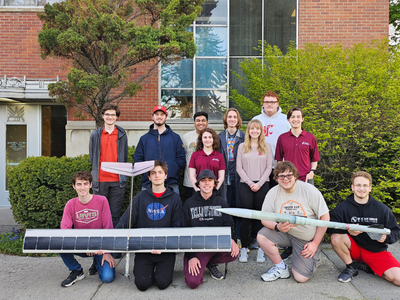 Students posing with a solar aerial vehicle and a small rocket.