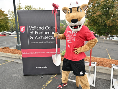 WSU mascot Butch T. Cougar holding a shovel by a sign with the Voiland College logo.