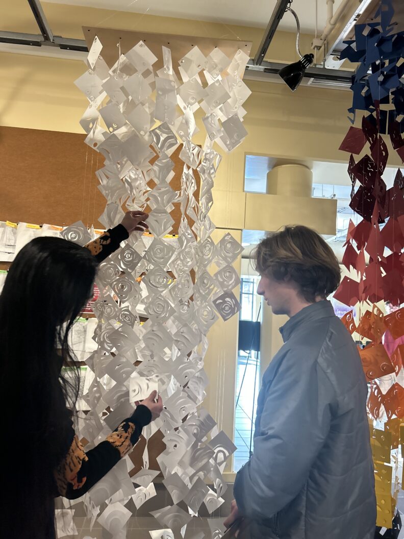 Two students looking at the clippings of permeable wall structure hanging from the ceiling.