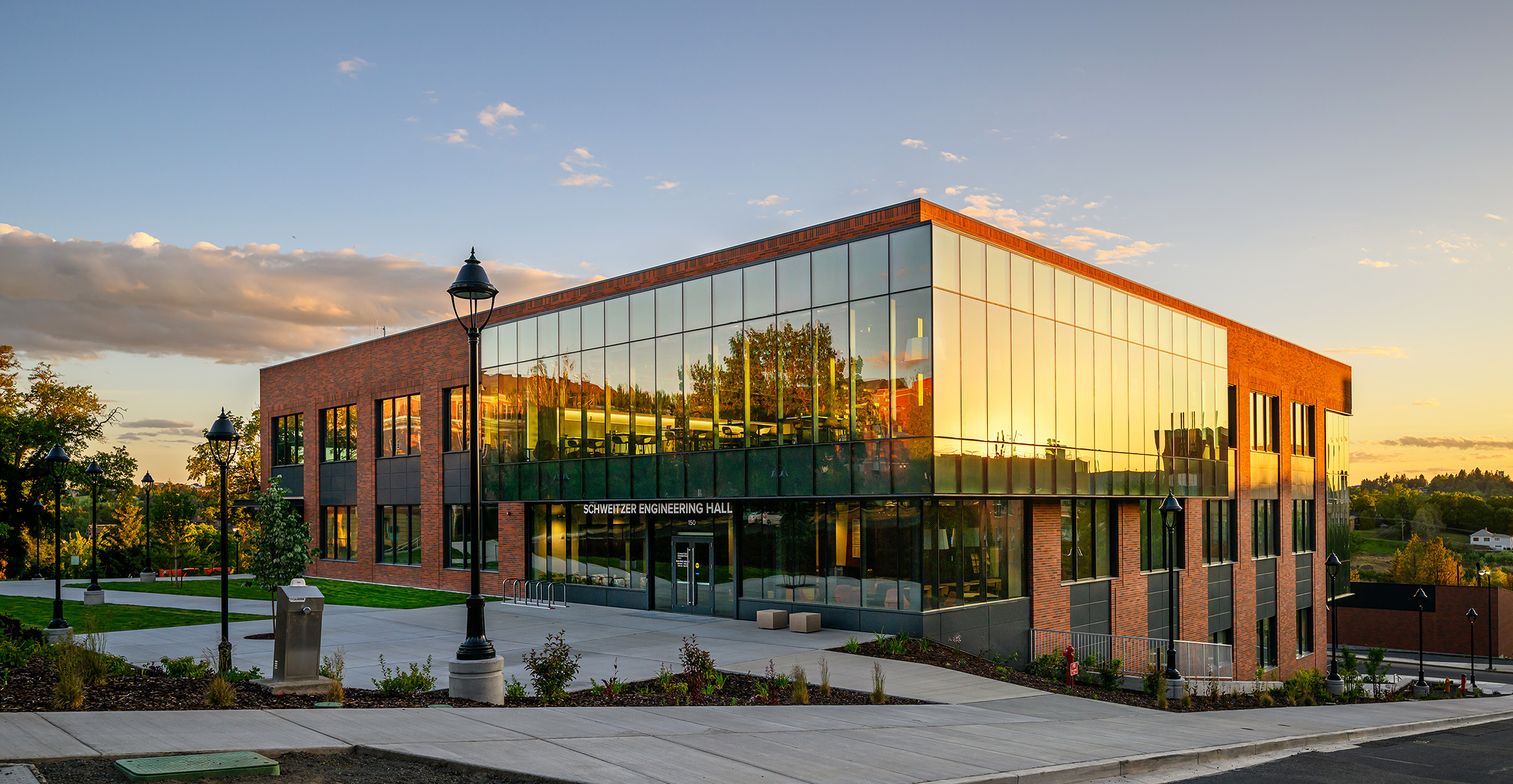 A glass and brick multi-story building at sunset with Schweitzer Engineering Hall above the door.