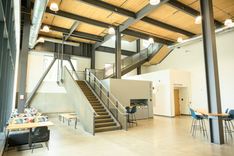 An interior space with tables, seating, a mini mart, and starts leading up.