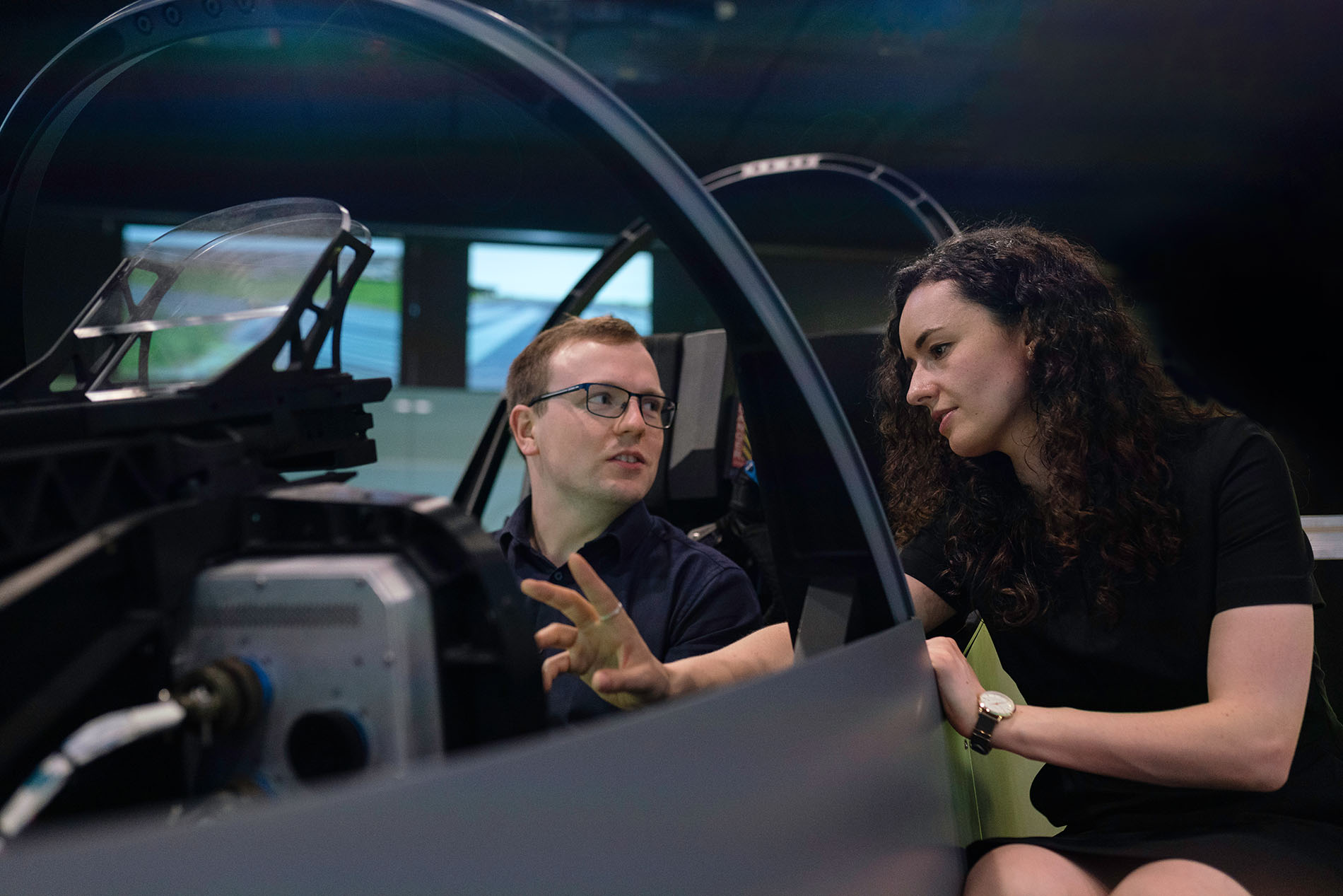 Two people looking at an airplane cockpit. One is sitting in the seat of the plane.