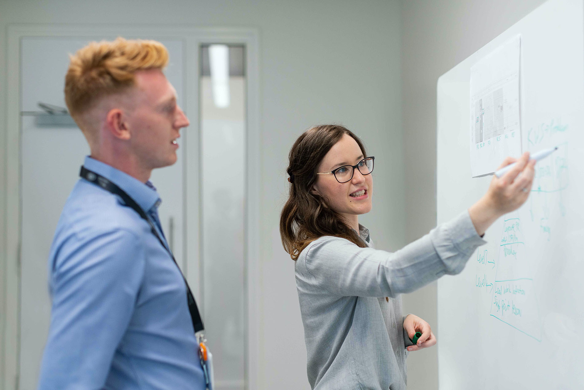 Two Engineers standing in front of white board discussing project.