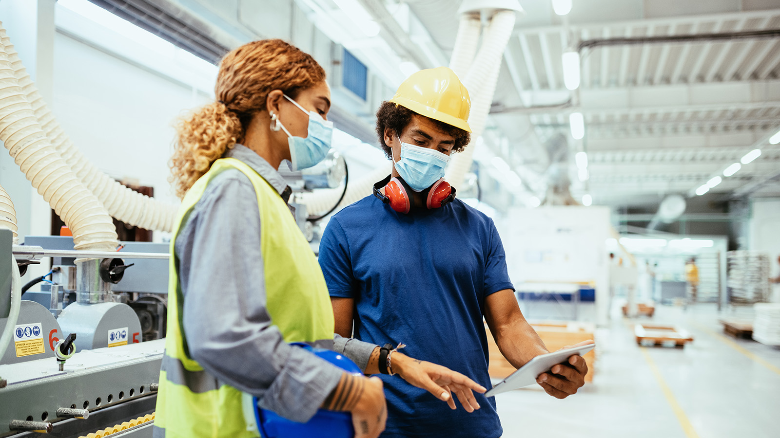 Engineers, architects and blue collar workers in protective clothing working in factory with modern machinery.