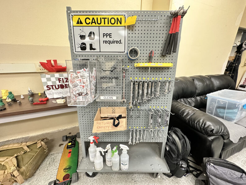 Peg board with tools, supplies, and a "PPE required" sign