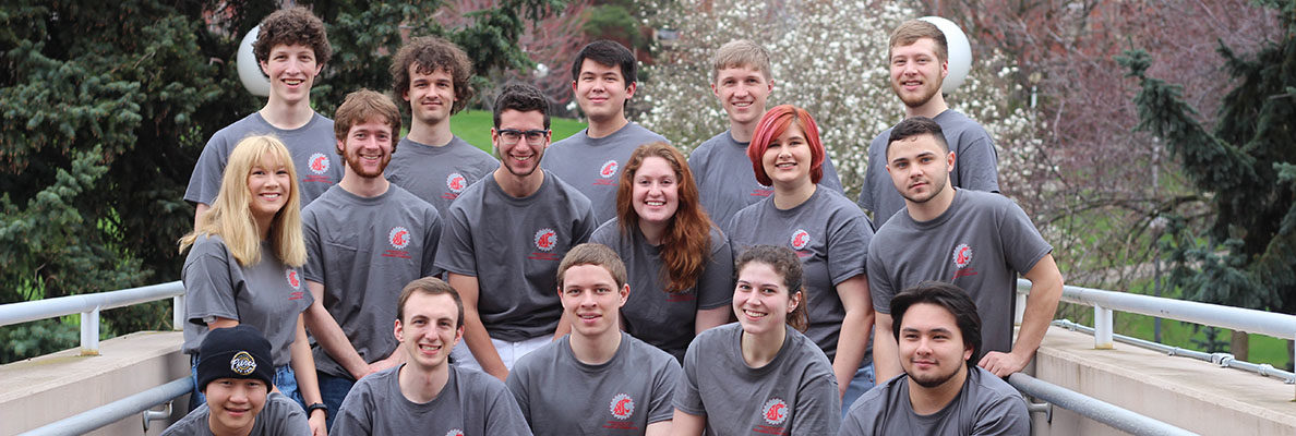 Sixteen robotics club members pose with a robot in front of Dana Hall in Pullman, WA.