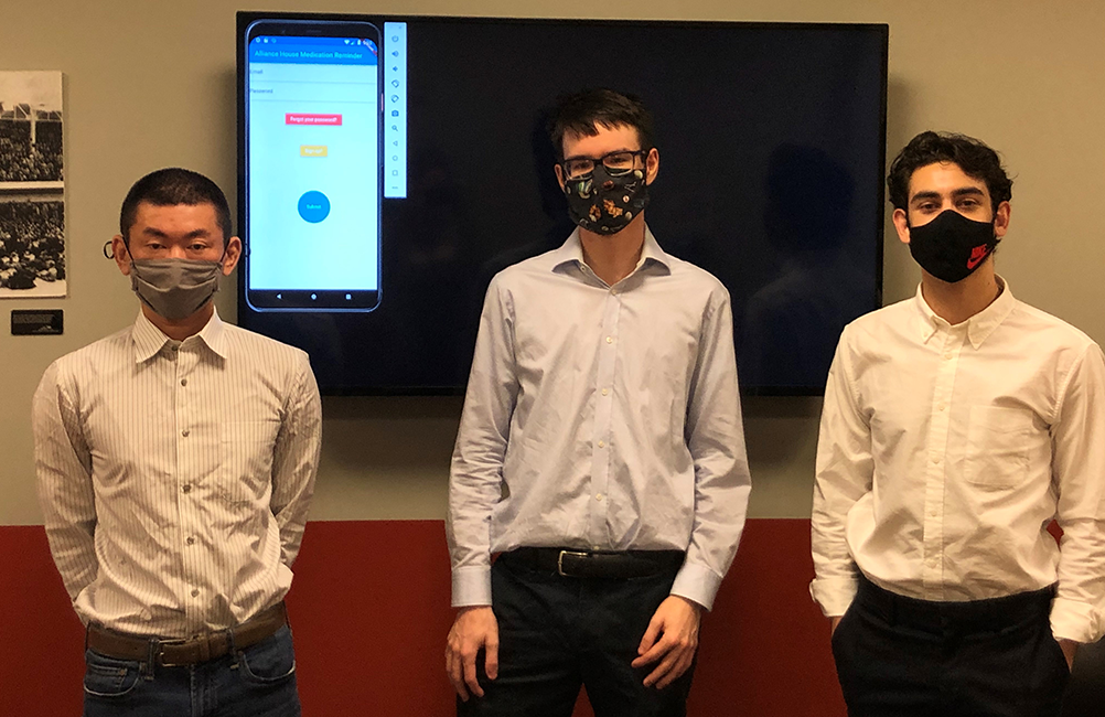 Three people wearing face masks in front of a screen showing their app.
