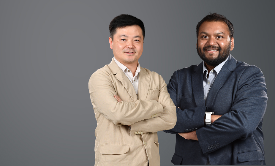 Two men posing in suits against a gray background.