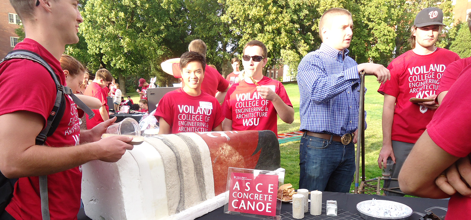 Students in Voiland College t-shirts displaying their concrete canoe at an outdoor event.