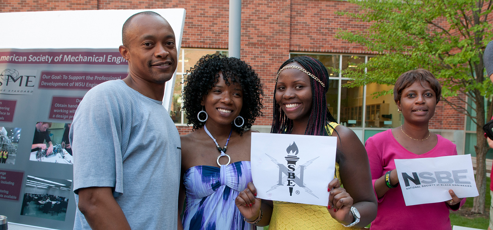 Four Black engineers holding signs with the NSBE logo.