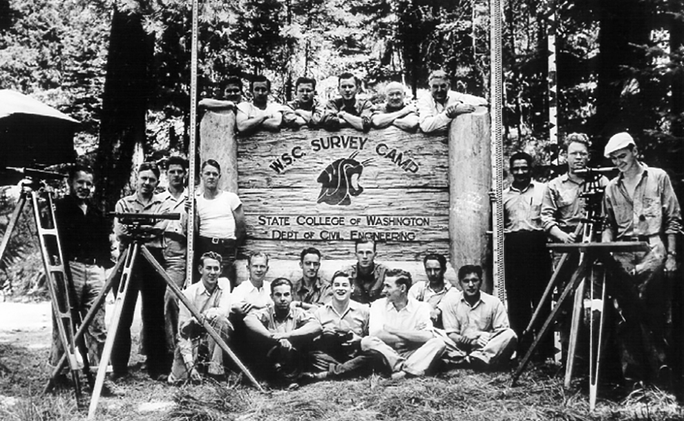 Historic photo of people around a sign that reads WSC Survey Camp, State College of Washington, Department of Civil Engineering.